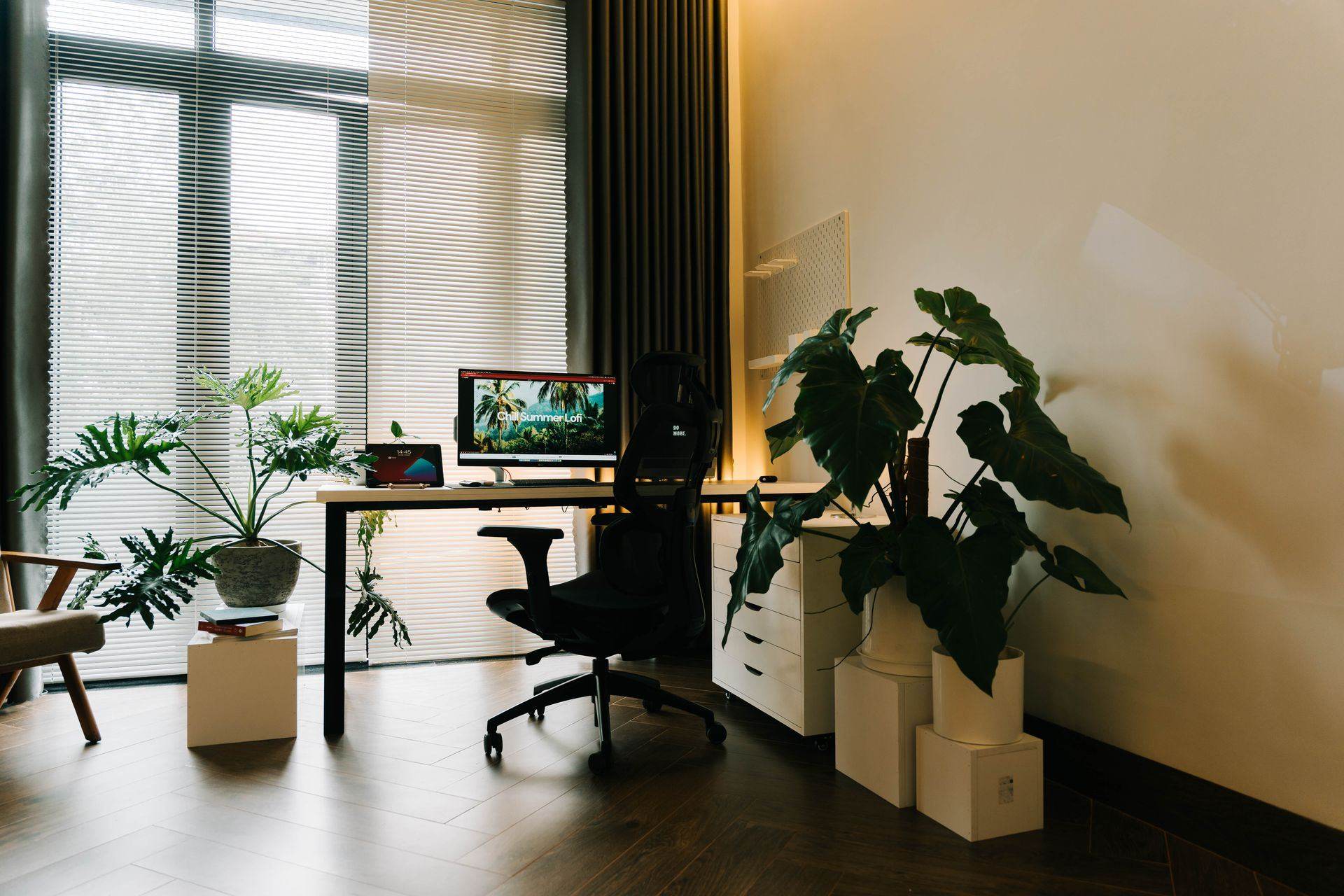 Home office con escritorio frente a la ventana, silla de oficina con respaldo de malla y plantas