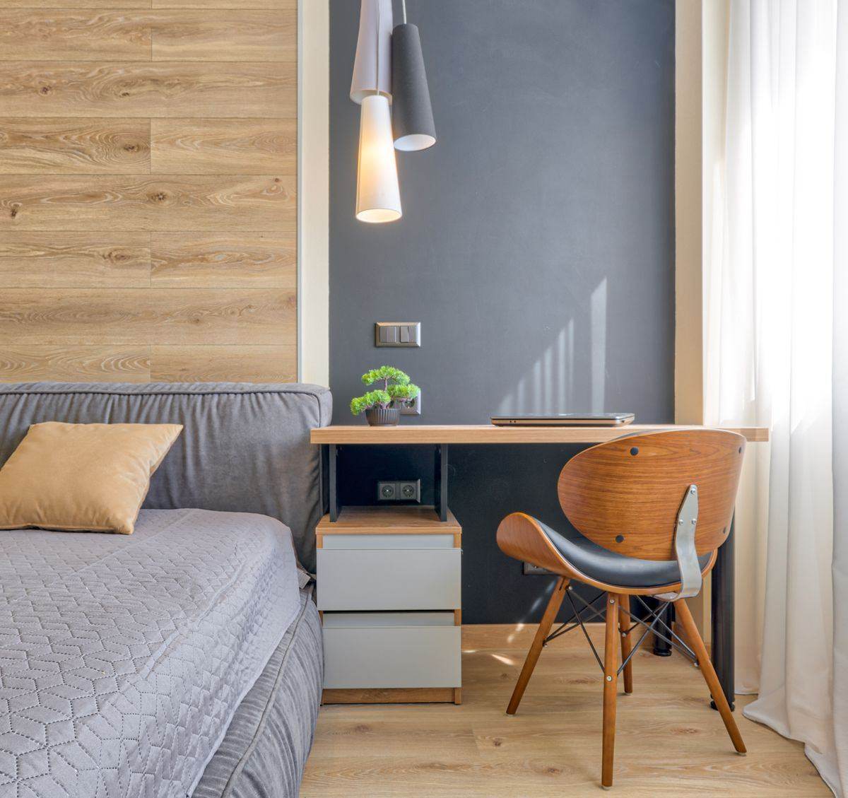 Rincón de trabajo en una recámara con escritorio de madera, silla de madera curvada y lámparas colgantes