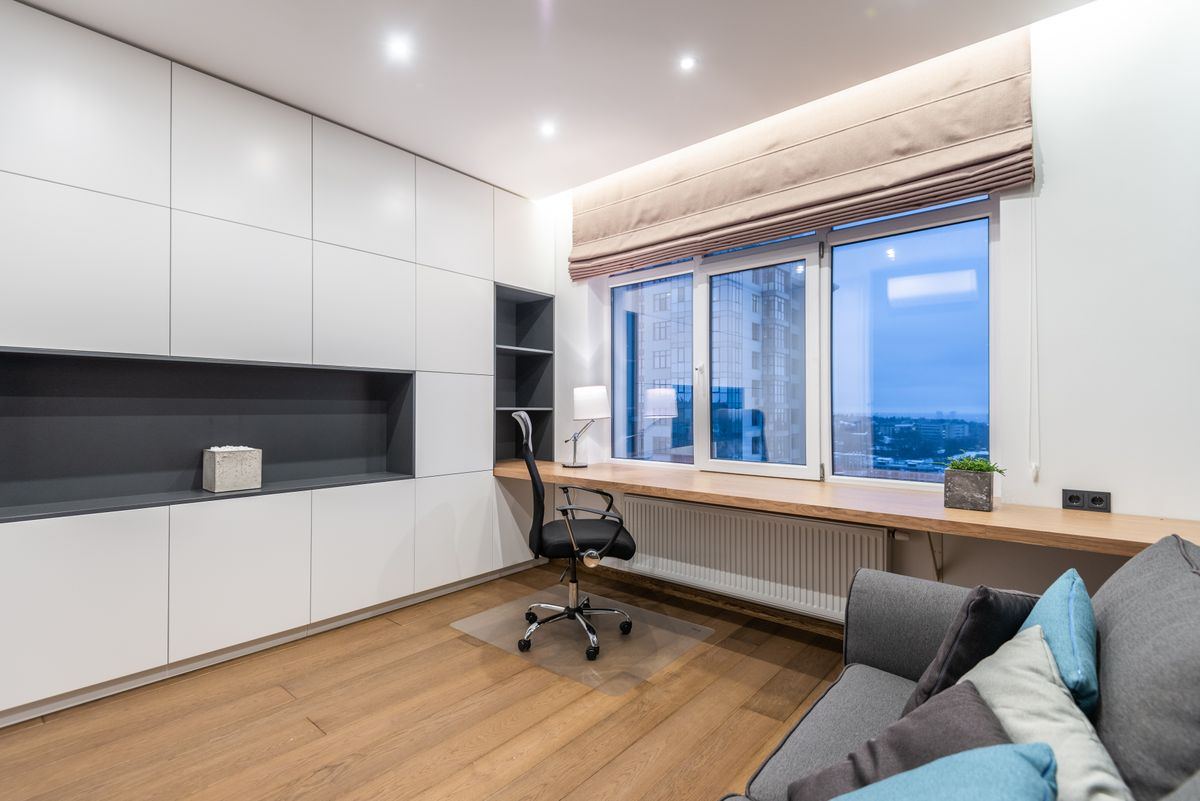 Estudio con muebles de guardado a todo lo largo de la pared y escritorio corrido bajo la ventana